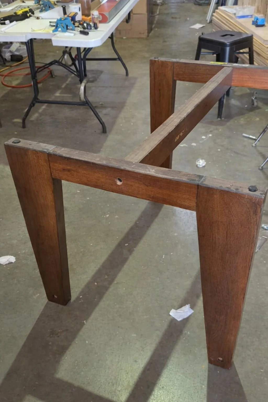 Move-damaged wooden dining-table base standing unstable in the workshop before structural reconstruction.
