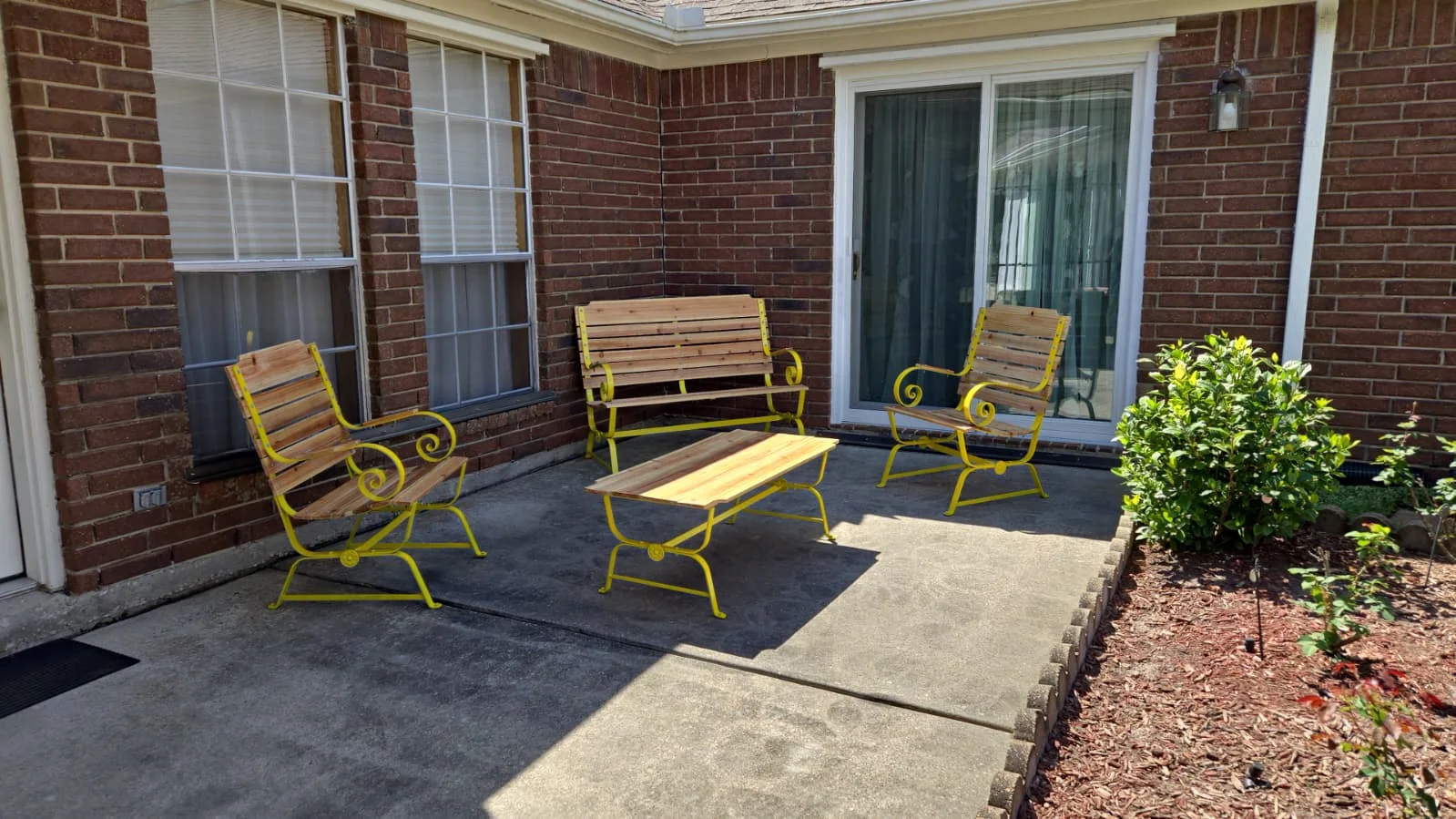 The fully restored yellow metal and warm cedar glider patio set arranged on a concrete backyard patio.