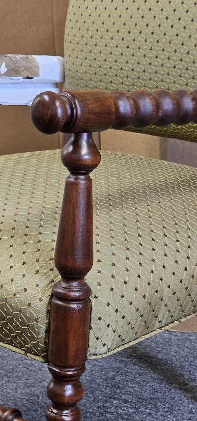 Close-up detail of a restored wooden armchair featuring clean green patterned upholstery and polished spool-turned armrests