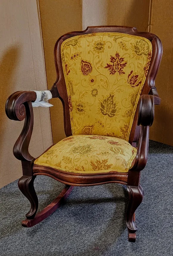 A fully restored wooden rocking chair with new yellow and red floral upholstery on the seat and backrest