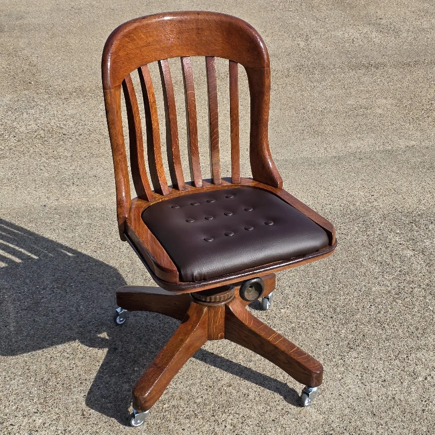 Restored vintage wooden swivel office chair with genuine leather upholstery and period-style casters.